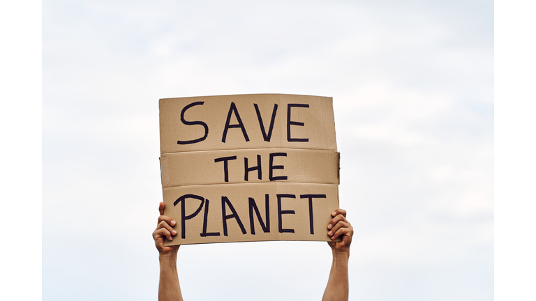 Unrecognizable man's hands holding a protest banner with the message SAVE THE PLANET, with the sky in the background.