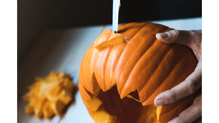 WOMAN'S HANDS WITH A KNIFE CUTTING A PUMPKIN PREPARING HALLOWEEN