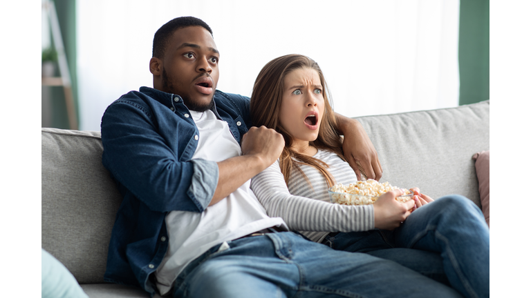 Horror Movie. Multicultural Couple Watching Scary Film And Eating Popcorn At Home