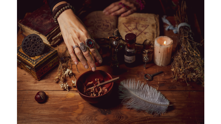 Female witch making potion on dark background, magic bottles with potions and candles on table of alchemist, Halloween theme
