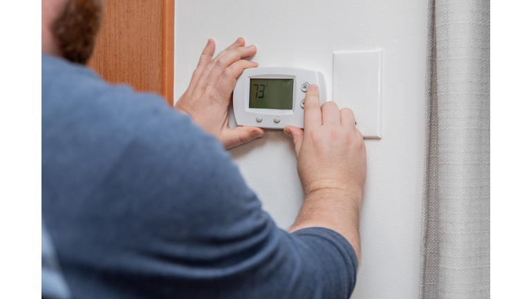 Man is pushing buttons and adjusting thermostat to change temperature at home