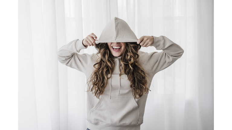 Playful woman covering eyes with hood at home
