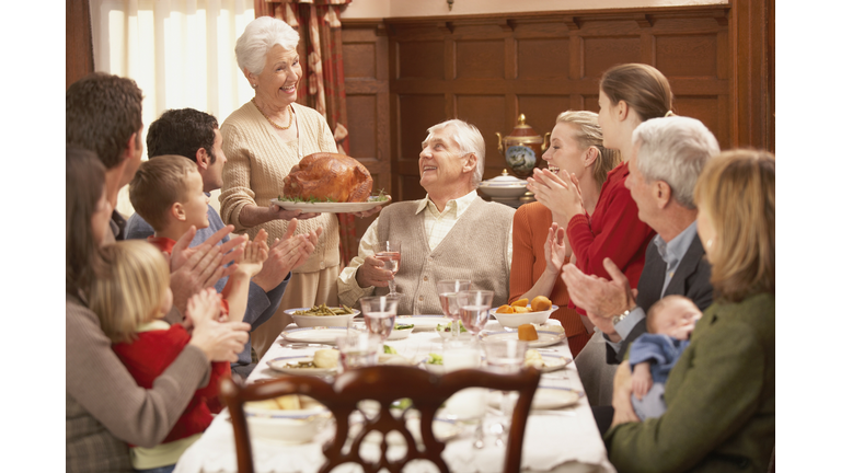 Grandmother presenting turkey to her family at the dinner table