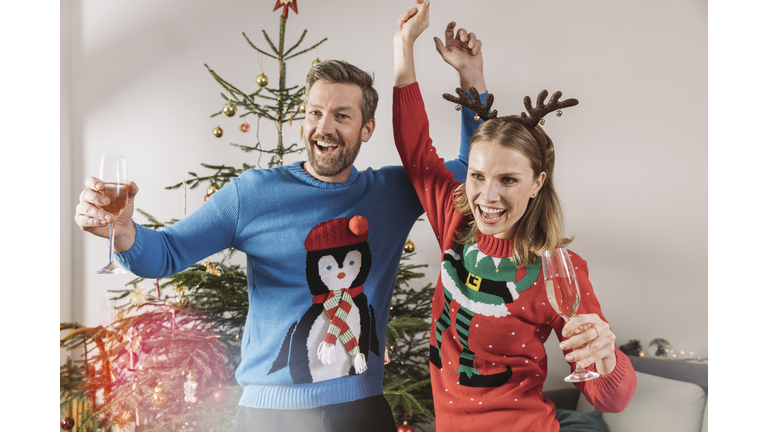 Two people with ugly Christmas sweaters dancing in front of tree