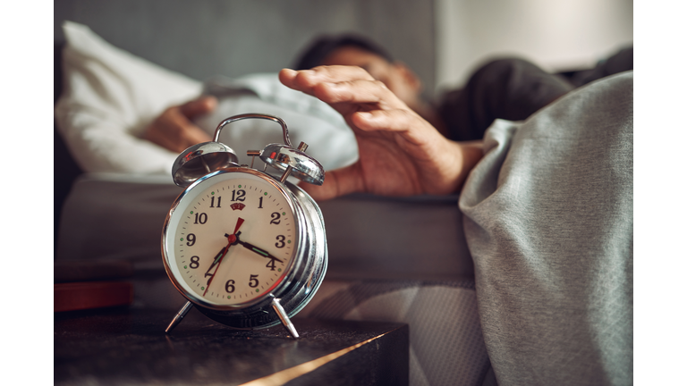 Shot of a young man reaching for his alarm clock after waking up in bed at home