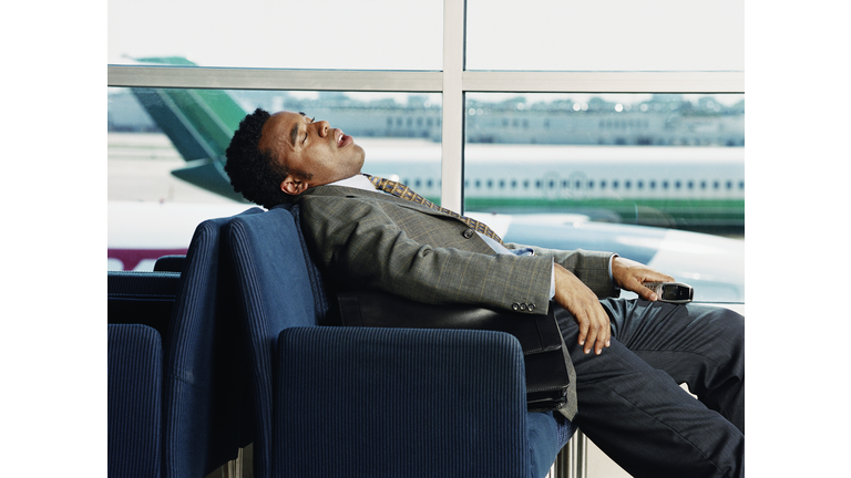 Businessman sleeping in airport lobby, side view
