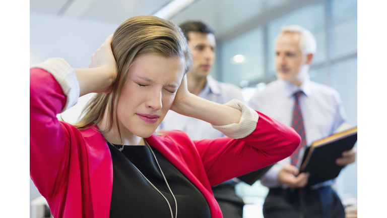 Female executive looking frustrated in an office with her colleagues discussing in the background