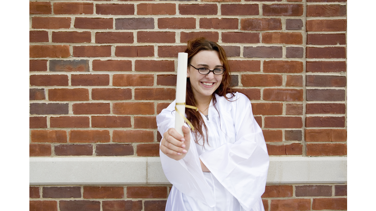 Young woman wearing graduation clothing, holding diploma, smiling