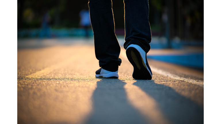 Low Section Of Man Walking On Street During Sunset