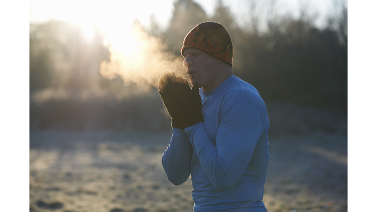 Runner wearing knit hat and gloves, rubbing hands together, breathing cold air