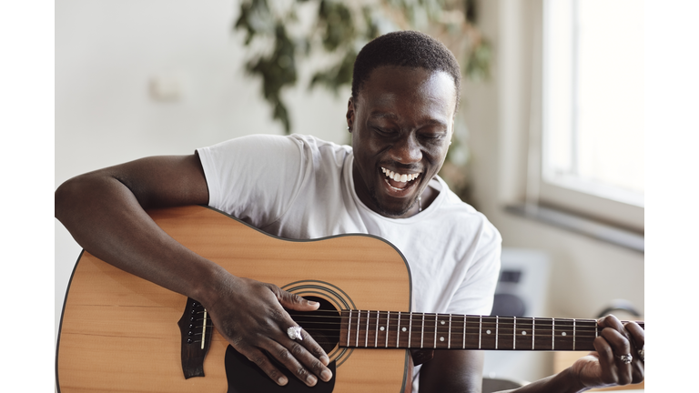 Happy male artist singing while practicing guitar in classroom