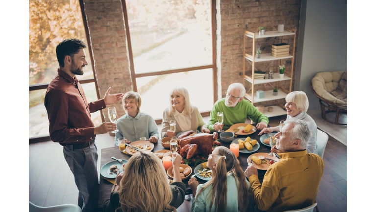 Photo of full big family gathering sit feast meals dinner table father guy telling thanksgiving pray toast multi-generation harmony in evening living room indoors