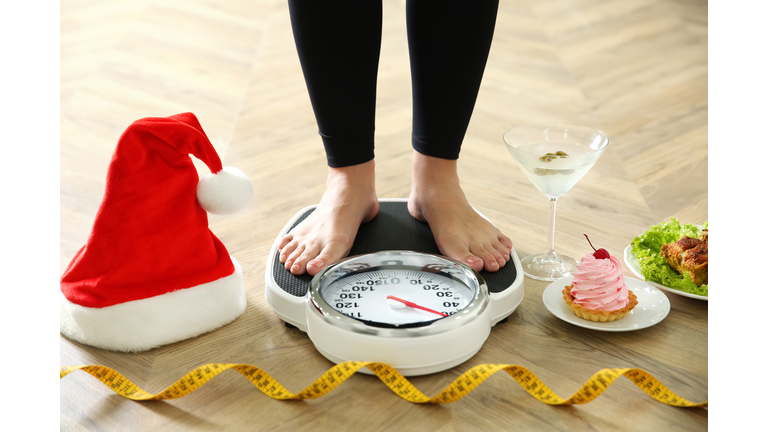 Food, alcohol left after Christmas holidays and woman with measuring tape standing on scales indoors, closeup. Overweight problem