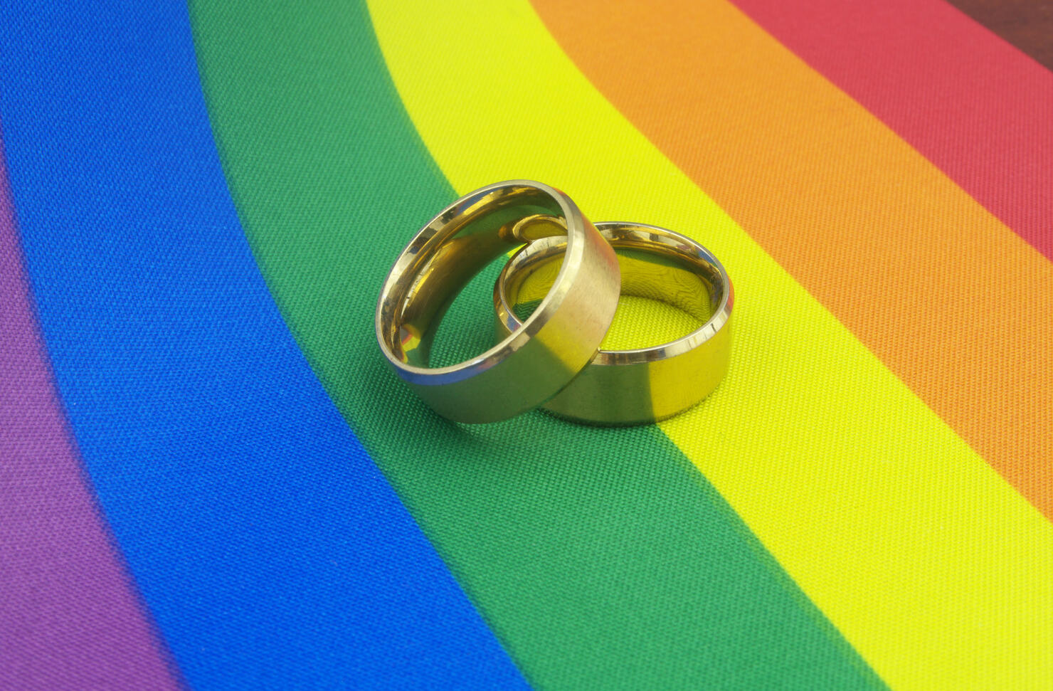 Gold wedding rings on LGBT pride flag.