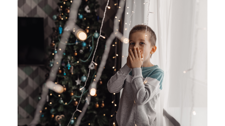 Beautiful little boy, lying down on the floor, looking at candles, making wishes for Christmas