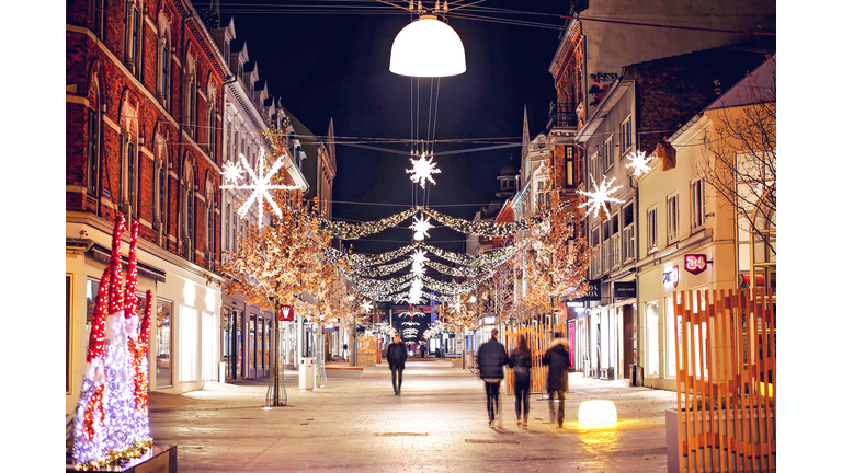 Blur Image Of People Walking On Street Amidst Illuminated Buildings Decorated With Christmas Lights