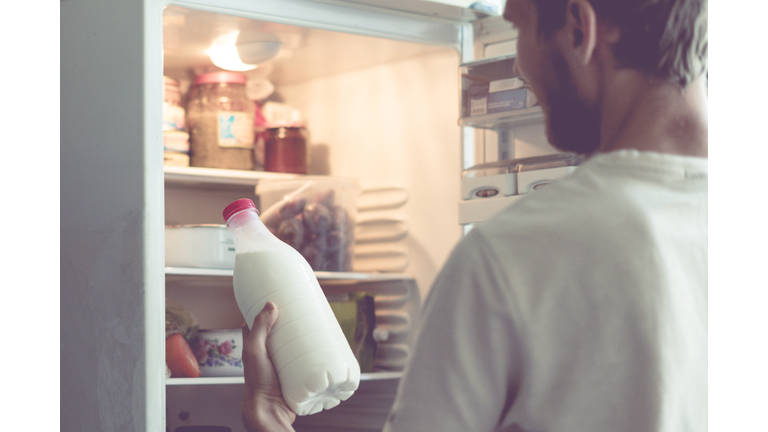 young bearded man opens the bottle of milk standing near fridge at home