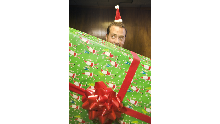 Mid adult man wearing santa hat, holding giant present with large bow
