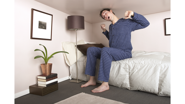 Man sitting on bed stretching in miniature bedroom