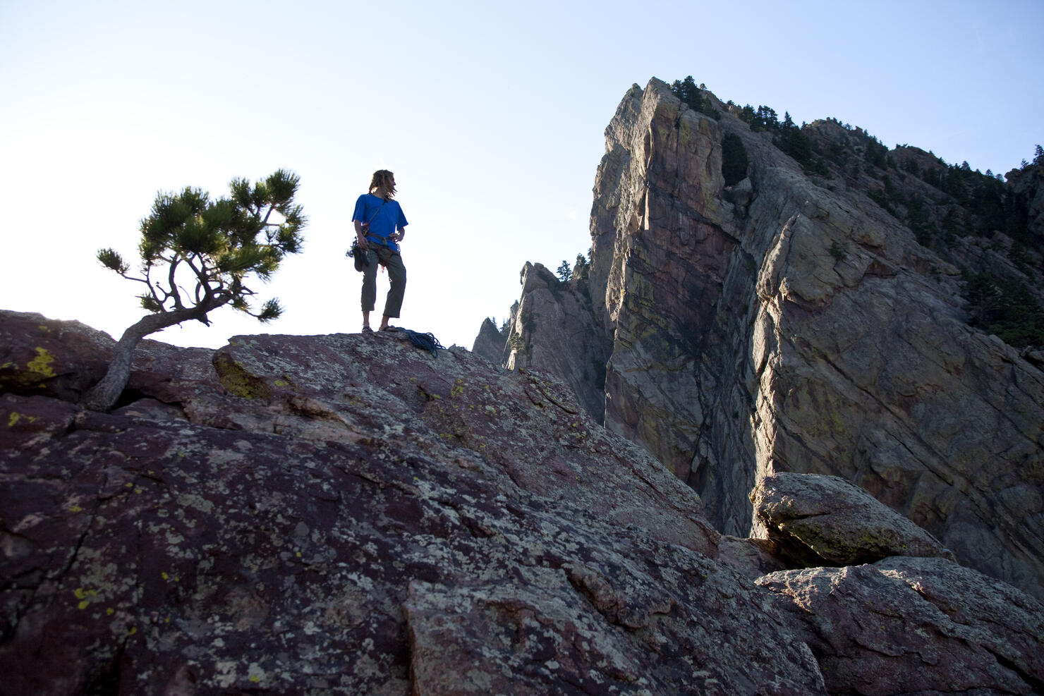A young adult stands triumphantly on top of a 500 ft multi pitch trad climbing route in Colorado.