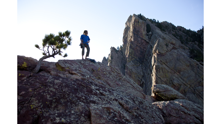 A young adult stands triumphantly on top of a 500 ft multi pitch trad climbing route in Colorado.