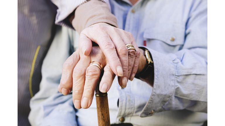 Close-up of old man's and woman's hands resting on a cane