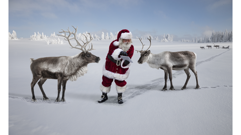 Santa Claus showing reindeer a map on tablet