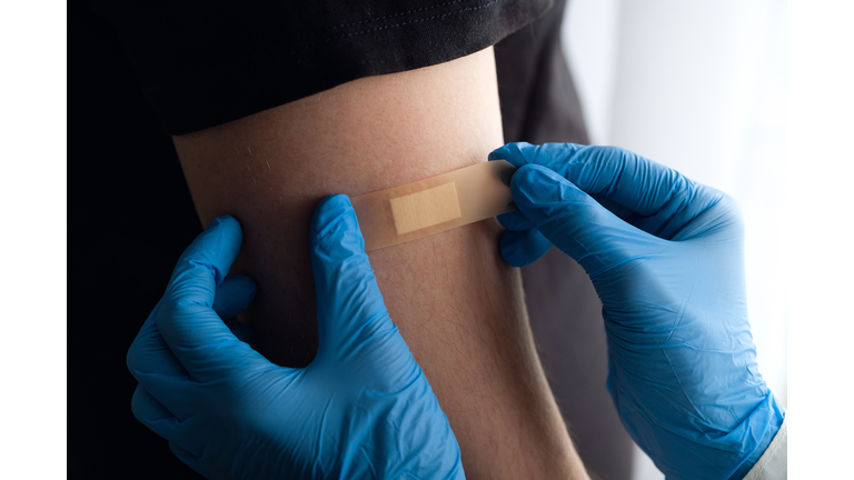 A woman Doctor wearing gloves or a medical professional applies a patch or adhesive bandage to a man's arm after vaccination or injection of the drug. The concept of medicine and health care, vaccination and treatment of diseases. First aid services.