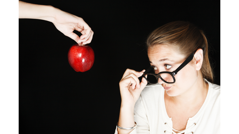 Serious, disapproving teacher looks over spectacles at offered apple