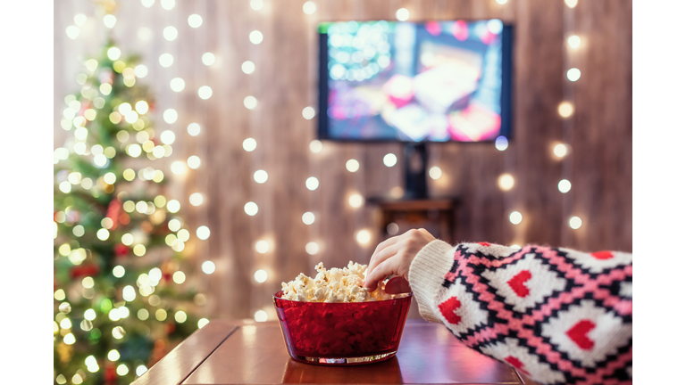 Christmas eve. Alone woman watching tv and eating popcorn. Home cinema. Cropped, close up