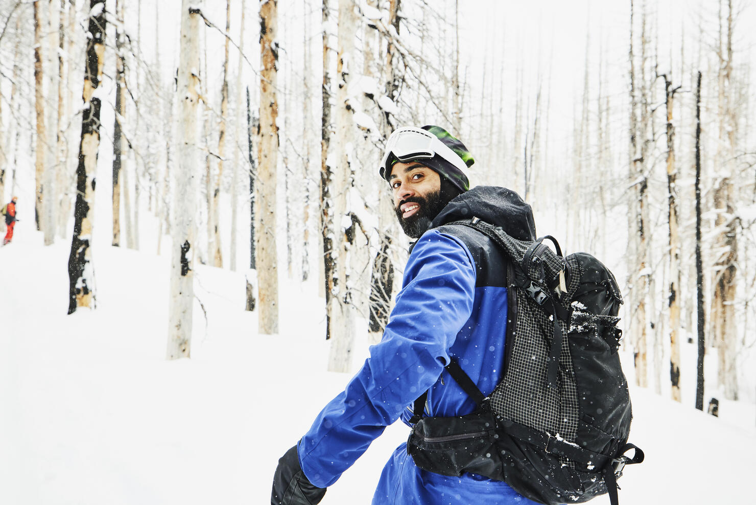 Portrait of smiling snowboarder traveling through snow covered burned forest on winter afternoon
