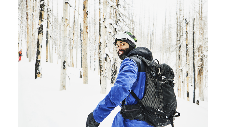 Portrait of smiling snowboarder traveling through snow covered burned forest on winter afternoon