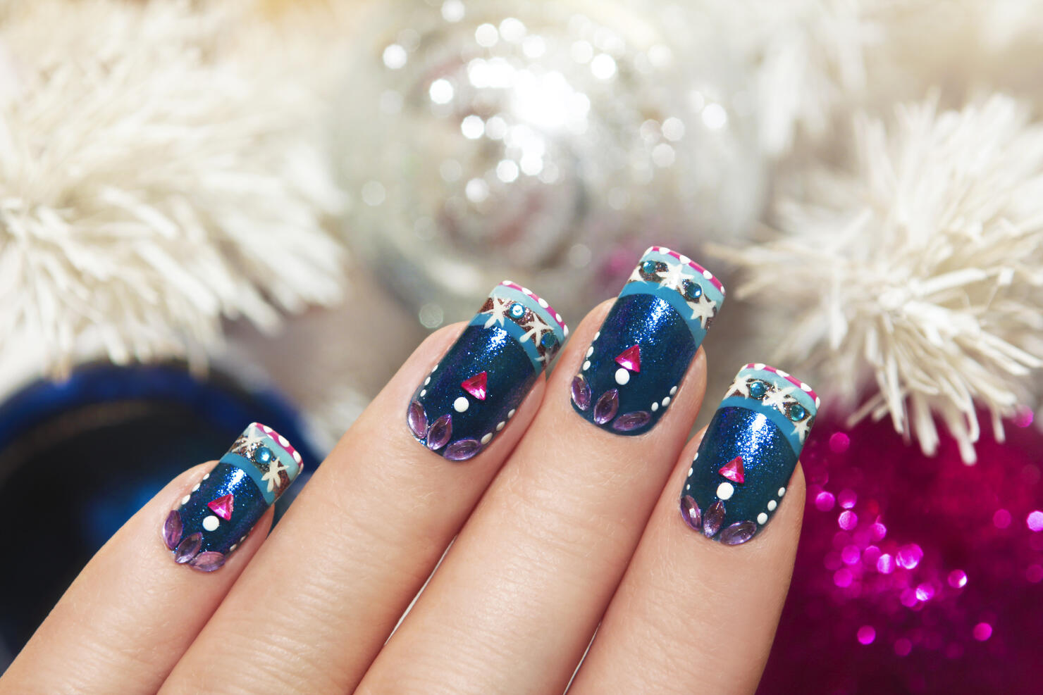 This stunning winter blue manicure has snowflakes and pink triangular rhinestones near the white tree and colorful shiny balls.