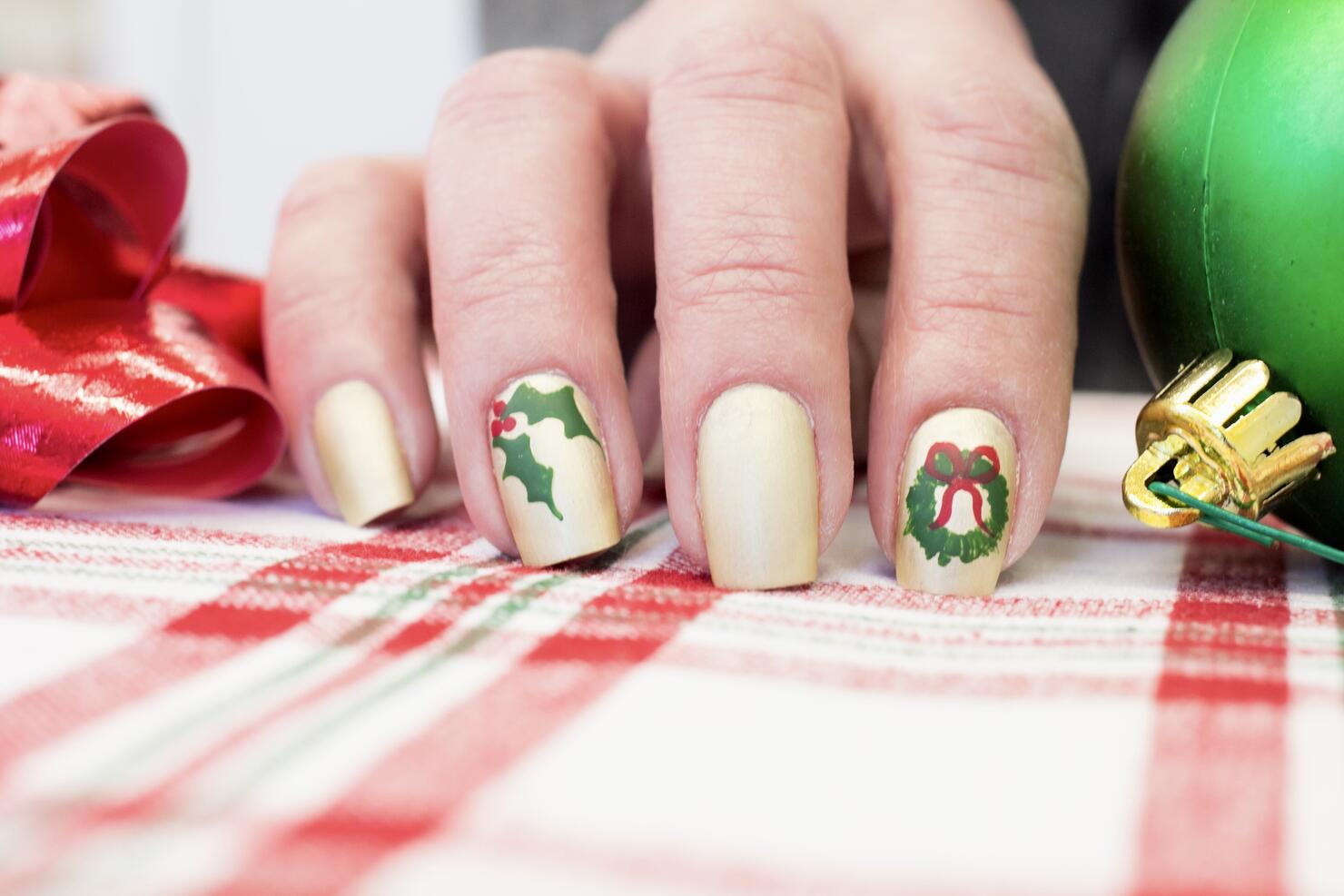 This holly and Christmas wreath design stands out on a classic gold nail polish.