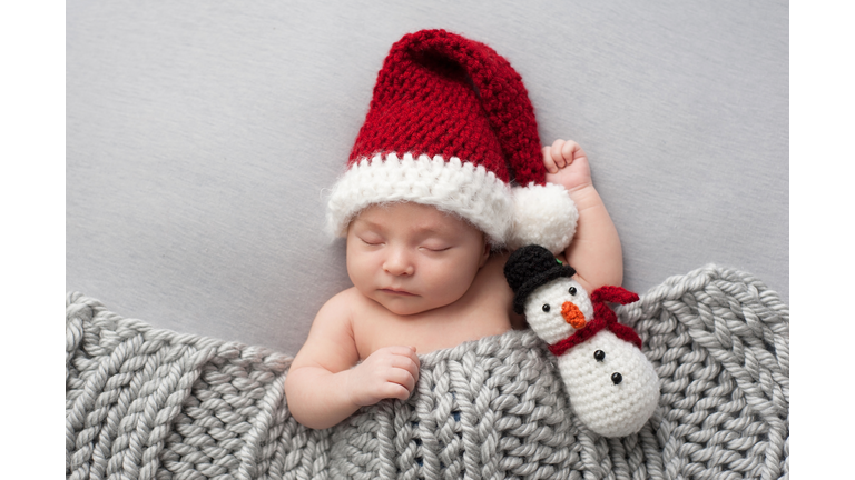 Sleeping newborn baby boy in Santa hat with plush snowman toy