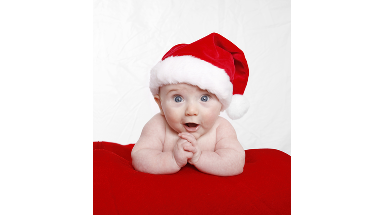 Surprised baby girl wearing a Santa hat on a red blanket