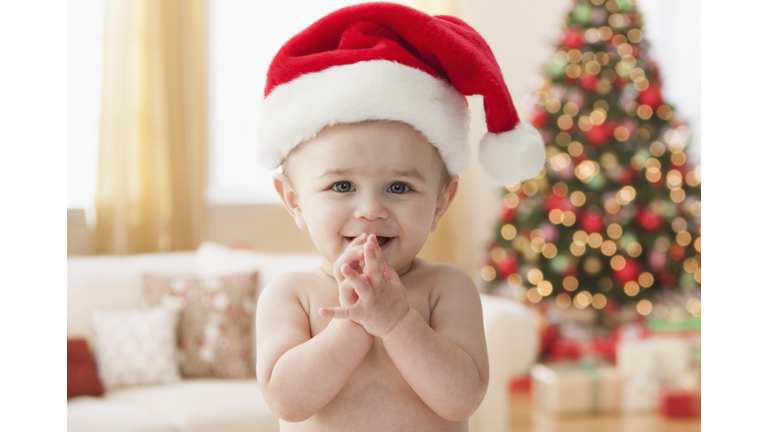 Baby in Santa hat smiling into clasped hands