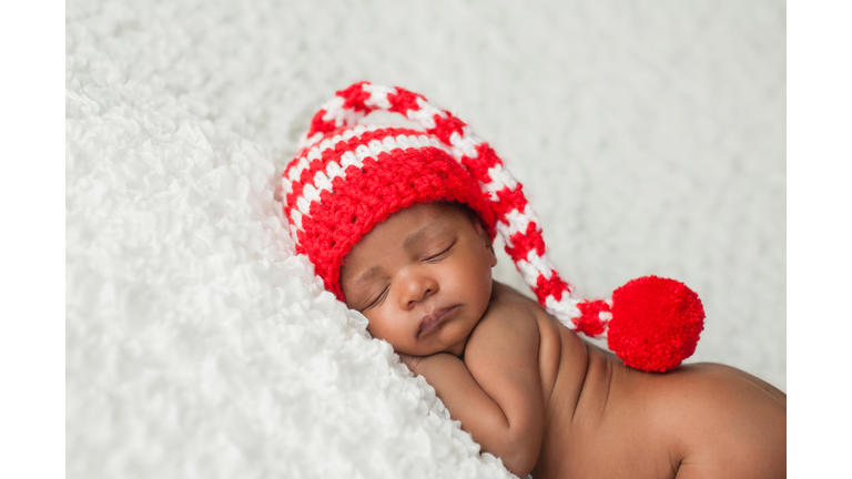 Baby asleep on white blanket wearing a Christmas striped hat