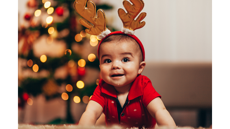 Cute baby boy wearing reindeer antlers with Christmas lights behind him