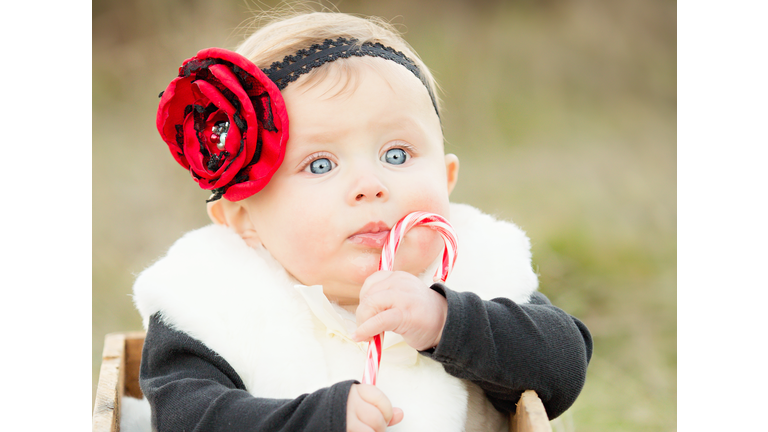 Adorable baby girl holding candy cane and wearing a red rose hair band