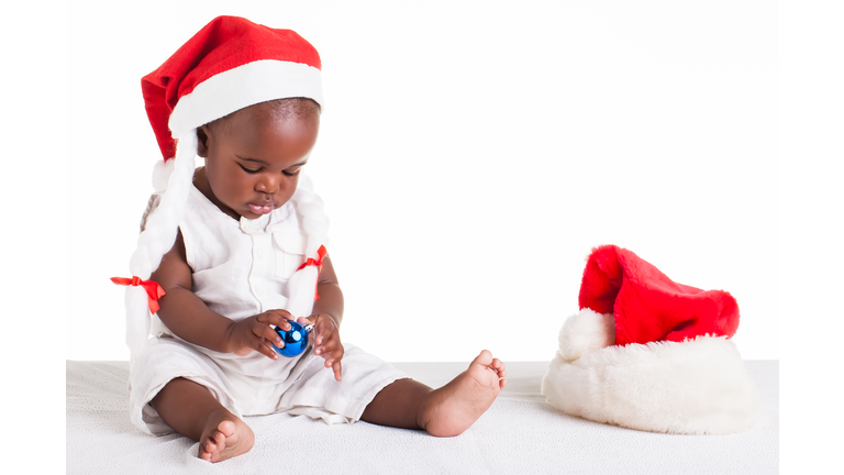 Cute baby boy wearing Santa hat and playing with a Christmas decoration