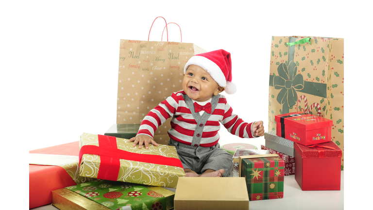 Adorable baby boy wearing Santa hat and surrounded by wrapped gifts