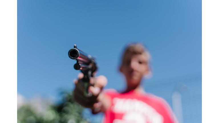Blonde teenager wearing a red t - shirt pointing with a gun.