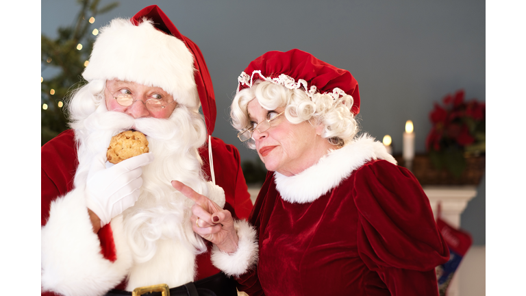 Mrs. Claus pointing on Santa eating gingerbread cookie