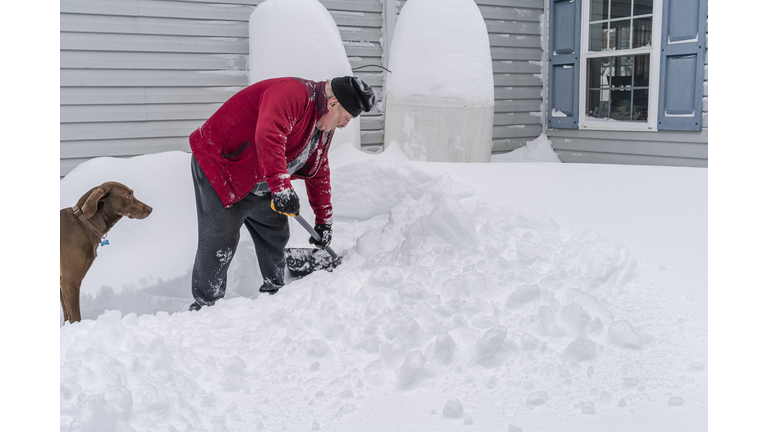 Senior man cleaning the snow after a snowfall around his house, making a way to propane tanks with ошы dog accompanied.