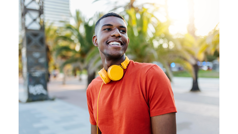 Happy man with headphones standing in the street while looking away