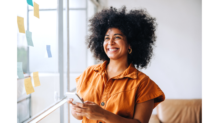 Happy black businesswoman using a smartphone in a creative office