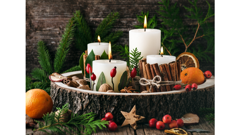 Christmas, advent wreath with four white burning candles decorated with natural material. Slices of fresh dried apple, orange and spices for cooking or baking.