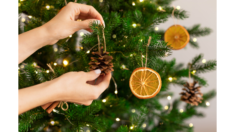 Female hands hanging handmade decoration on Christmas tree.