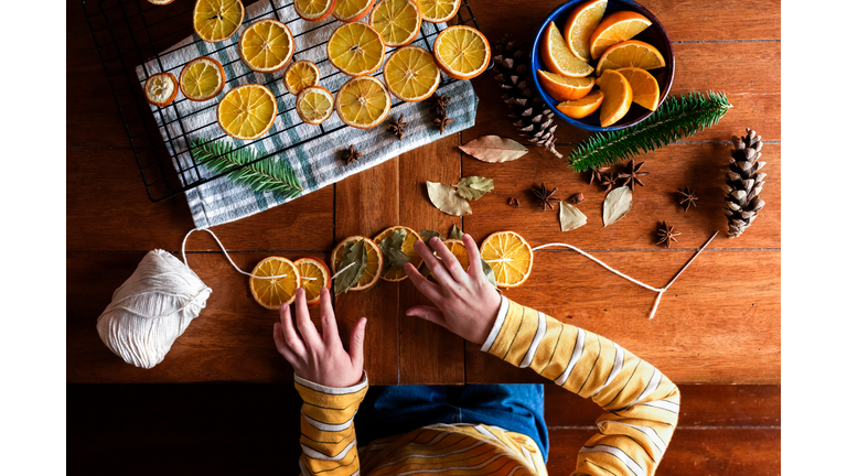 Childs hands putting together dried orange garland for Christmas